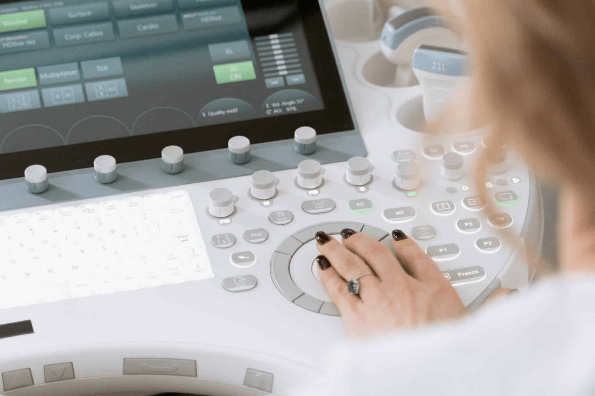 A woman operates a computer to manage an ultrasound machine, focused on the screen in a clinical setting.