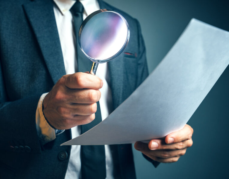 F2 Tech Notes - A man dressed in Suit Holding a Magnifying Glass an a Paper